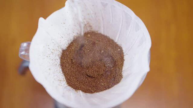 Brewing coffee with the v60 method. Water is poured from a kettle into a glass cup through a coffee filter, water is mixing with ground coffee beans