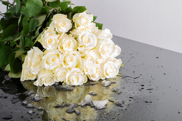 A bouquet of white beige 19 roses with water drops on a mirror table with a snow, ice and beautiful reflection. Symbol of love and Valentine's Day. Floral gift for wedding, mother's day, birthday