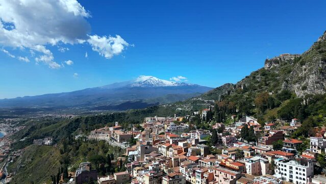 Taormina, Sicily, Italy. Cityscape drone aerial view. Old Greek theatre ruins with active eruption volcano Etna background. Popular travel destination in Europe, UNESCO historical heritage