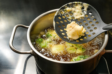 Deep frying cauliflower and broccoli wrapped with beer batter in a pot with hot boiling oil on a...