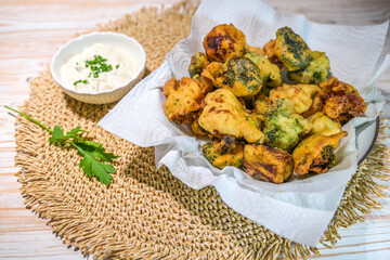 Crispy vegetables such as broccoli and cauliflower deep-fried in beer batter with a yogurt dip on a...