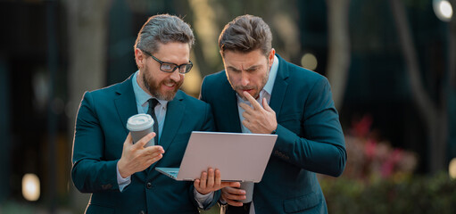Handsome business man in suits working on laptop and communication with business projects in city. Partners thinking and plan for business. Business men team using laptop outdoor.