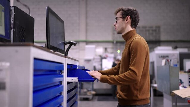 Video of an engineer using computer to change the inventory picking up a piece of metal in a cnc modern factory