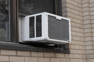 exterior view of air conditioning window unit extruding from the window sill of a beige brick building