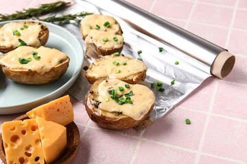 Tasty baked potato with cheese and aluminium foil roll on color tile background, closeup