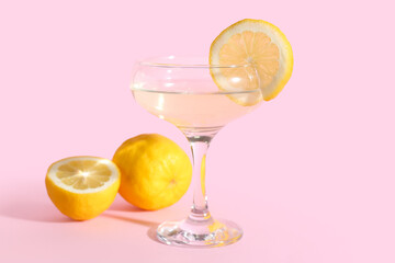 Glass of tasty martini and lemon on pink background