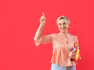 Mature female teacher of Spanish pointing at something on red background