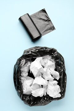 Black roll of garbage bags and rubbish bin with crumpled paper on blue background