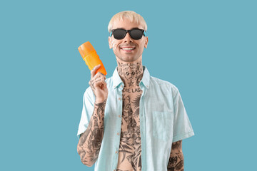 Tattooed man with sunscreen cream on light blue background