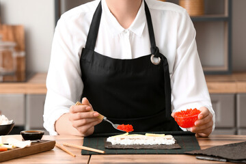 Woman preparing delicious sushi rolls in kitchen