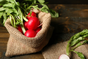 Sack bag of ripe radish with green leaves on wooden background, closeup