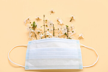 Medical mask with blooming branches on beige background. Seasonal allergy concept
