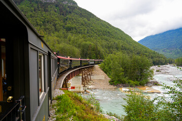 Fototapeta premium Narrow-gauge train of the White Pass and Yukon Route on an old trestles bridge in the Alaskan mountains between Skagway and Canada