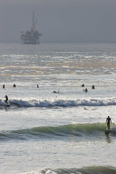 Beachgoers and surfers enjoy the ocean, while an oil platform sits off the coast in the background, Santa Barbara, California
