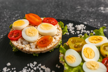 Rice crackers with quail eggs, tomatoes and lettuce on dark grunge background, closeup