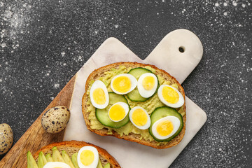 Tasty toasts with quail eggs, avocado and cucumber on dark grunge background