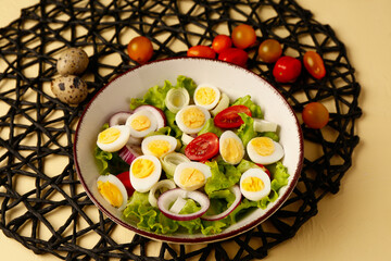 Tasty salad with quail eggs, tomatoes, onion and lettuce on beige background