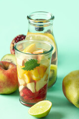 Glass and bottle of infused water with different sliced fruits on blue background