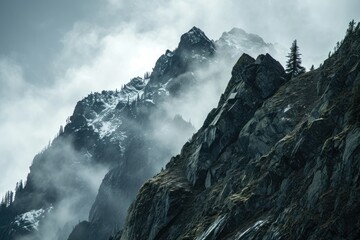 A majestic mountain range towers over a foggy landscape, its snowy peaks reaching towards the sky in a breathtaking display of nature's grandeur - obrazy, fototapety, plakaty