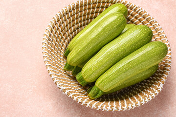 Wicker bowl with fresh green zucchini on beige background