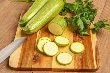 Board with slices of fresh zucchini and parsley on wooden background