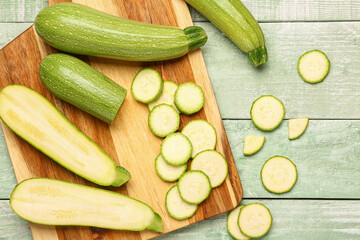 Board with slices of fresh zucchini on green wooden background