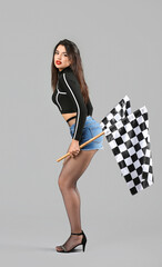 Beautiful young woman with racing flags on grey background