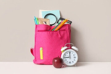 Pink school backpack with different stationery, alarm clock and fresh apple on white table near...