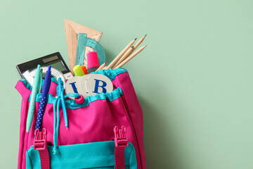 Colorful school backpack with different stationery on pale green background