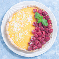 Lemon tart, garnished with fresh raspberry, icing sugar, mint, on plate, top view, square format