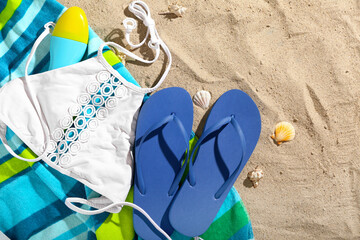 Pair of blue flip flops with swimsuit and blanket on sandy background
