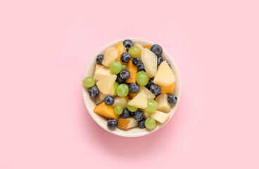 Bowl with fresh fruit salad on pink background