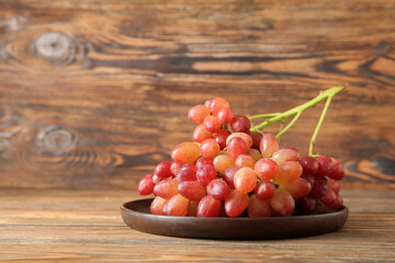 Plate with tasty ripe grapes on wooden background