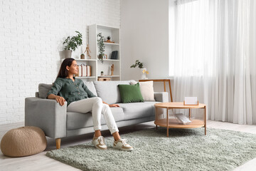 Beautiful happy young woman relaxing on sofa in living room - obrazy, fototapety, plakaty
