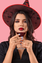 Young witch with drink on pink background, closeup