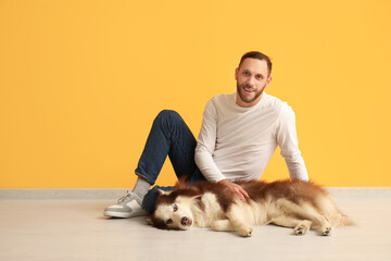 Handsome young man with cute Husky dog near orange wall