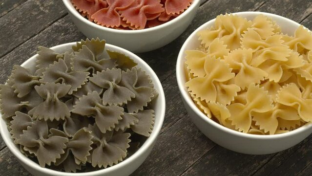Italian tricolore farfalle pasta. Different colors are separated into three bowls. Table spin.