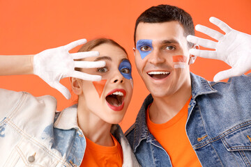 Young couple with painted faces on orange background, closeup