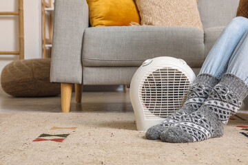 Woman in warm socks with electric fan heater at home
