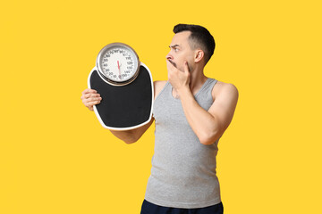 Handsome sporty shocked man with scales on yellow background. Weight loss concept