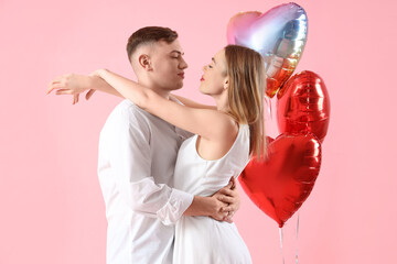 Happy young couple with beautiful heart-shaped balloons on pink background. Valentine's Day...