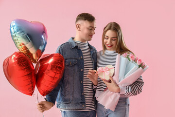 Happy young couple with heart-shaped balloons, bouquet of flowers and gift box on pink background....