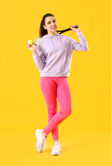 Young woman with tennis racket and ball on yellow background