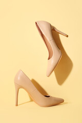 Stylish nude high-heeled shoes on color background