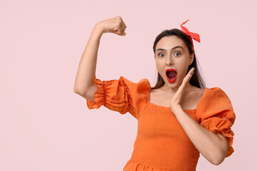 Beautiful surprised pin-up woman showing her muscles on pink background