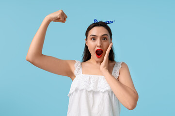 Beautiful surprised pin-up woman showing her muscles on light blue background