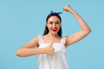 Beautiful happy pin-up woman showing her muscles on light blue background