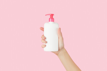 Womans hand holding white bottle on pastel pink background