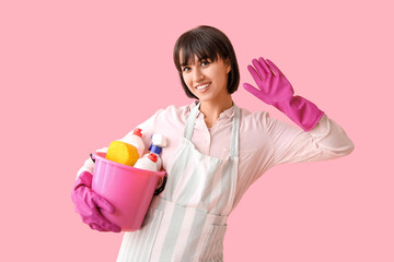 Young woman with cleaning supplies on pink  background