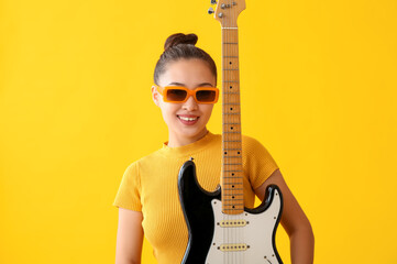 Young woman with electric guitar on yellow background - obrazy, fototapety, plakaty